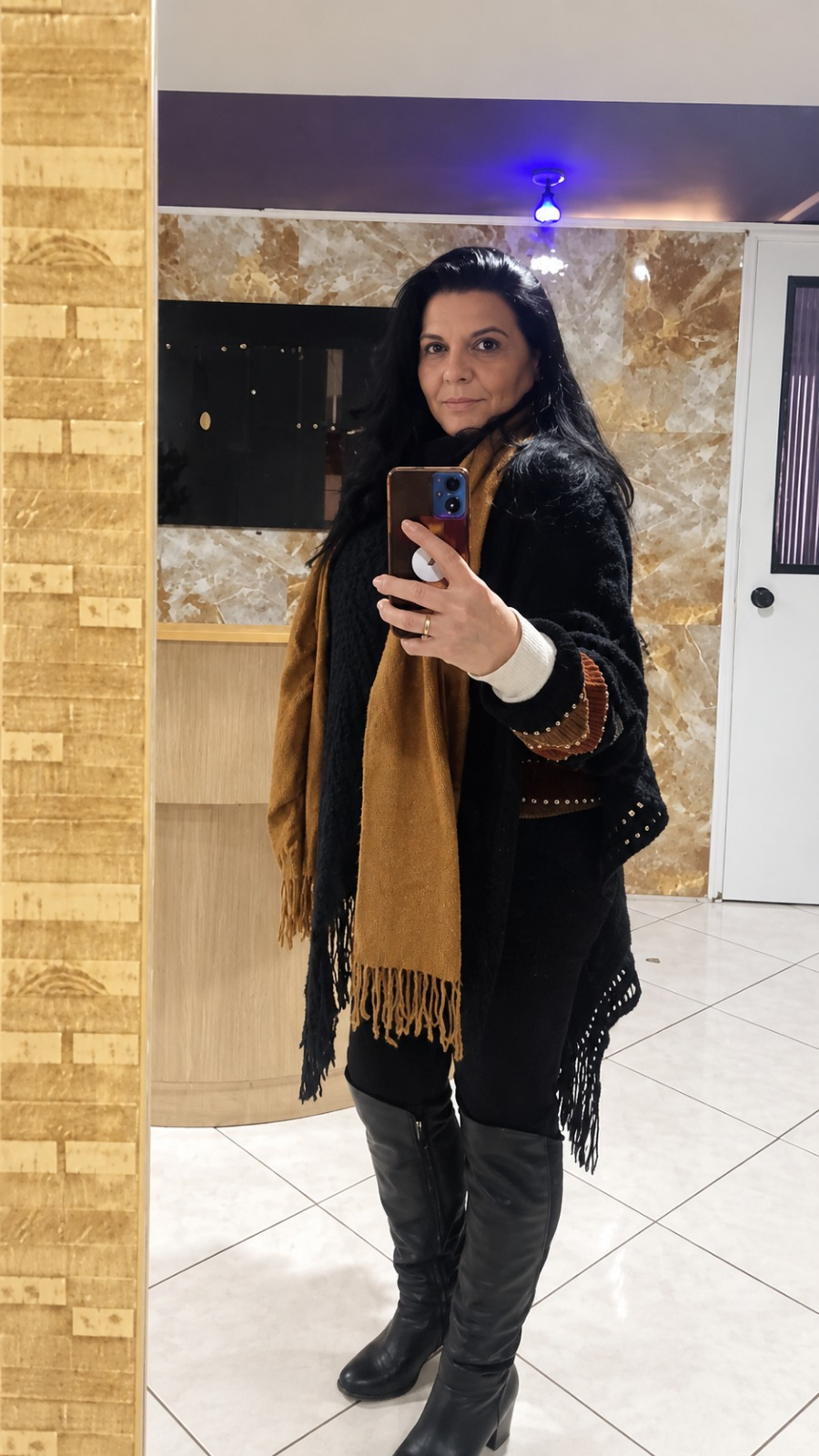 Monique em frente ao espelho, usando um casaco preto e cachecol caramelo